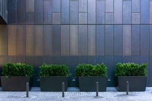 four anthracite grey planters with green plants growing and bollards in front in a commercial setting