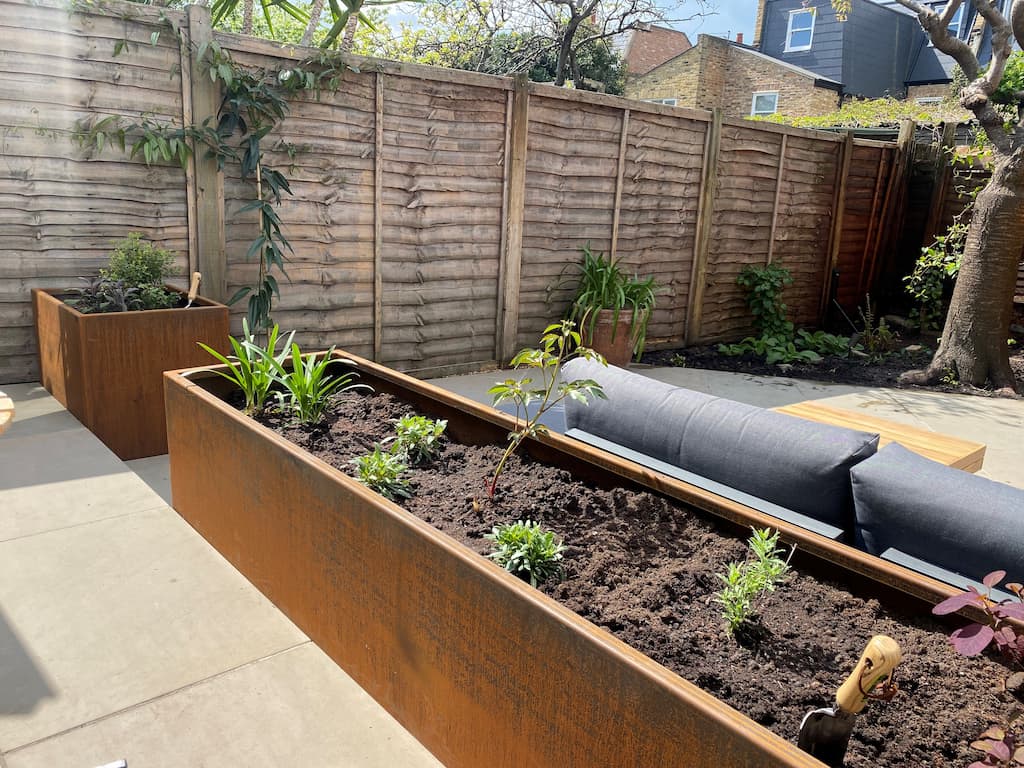 outdoor garden patio with two rusted steel planters with a wooden fence and sofa behind them