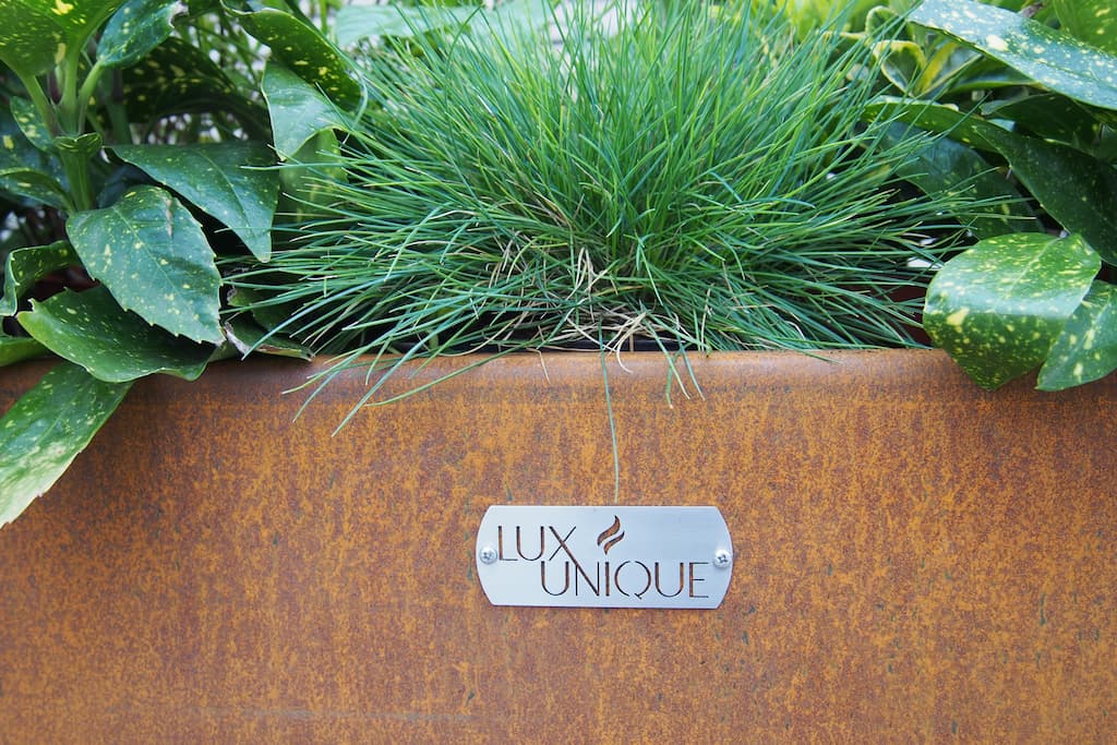 green plants growing inside a corten planter with an oranage patina and a lux unique branded bade of the front