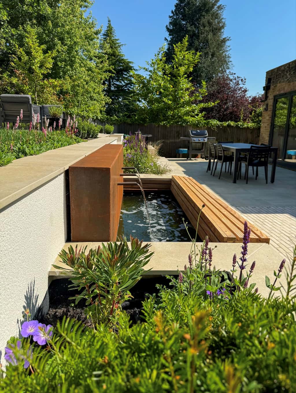 Corten water wall with 3 spouts Corten steel water wall feature including 3 spouts with water flowing out in a garden setting