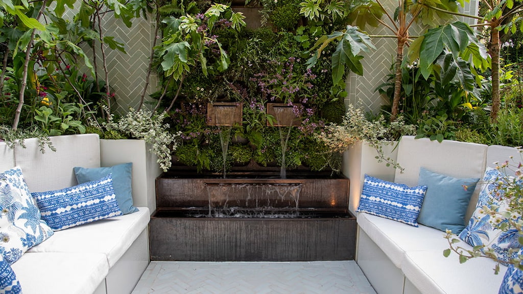 RHS chelsea 2024 bespoke water feature Corten steel water feature with water flowing and seats on either side with green plants in the background at the RHS Chelsea flower show 2024