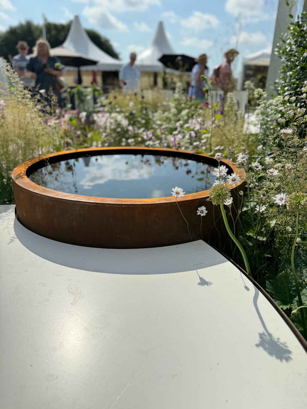 RHS show garden circular corten pond A circular corten steel pond with plants growing around it and people in the background