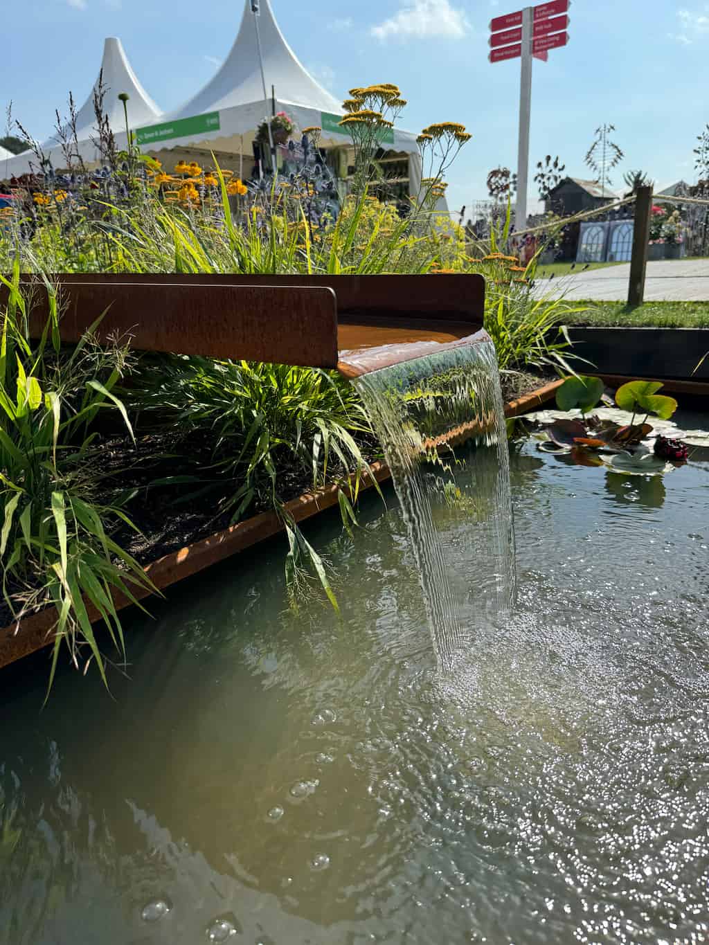 RHS show garden corten steel rill 3 A corten water rill with water flowing into a pond below and green plants in the background at a garden show