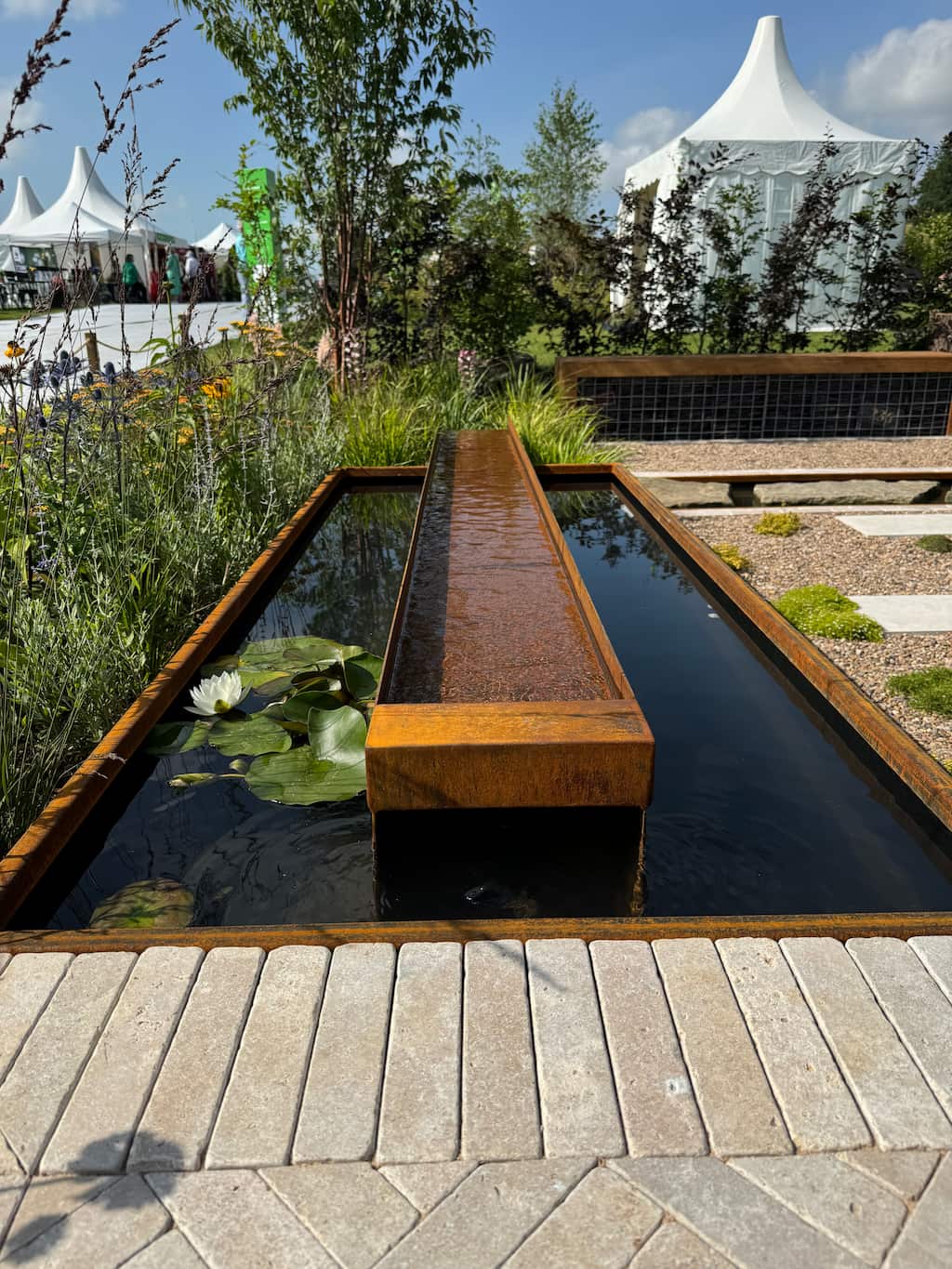 RHS show garden corten steel rill and pond Rusty steel water rill inside a rusty steel water pond with water inside and green plants in the background