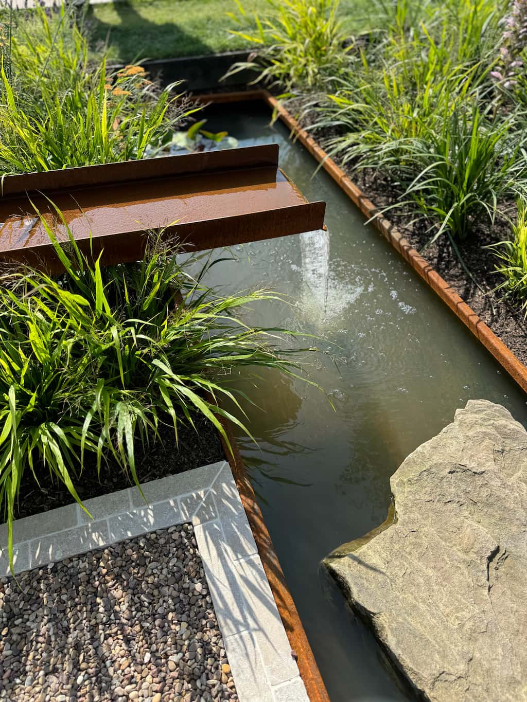 RHS show garden corten steel rill Corten steel rill with water flowing into a corten steel water pond with green plants on either side