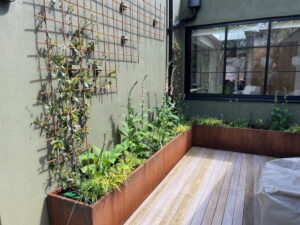 corten steel L-shaped trough planter with planting in courtyard garden